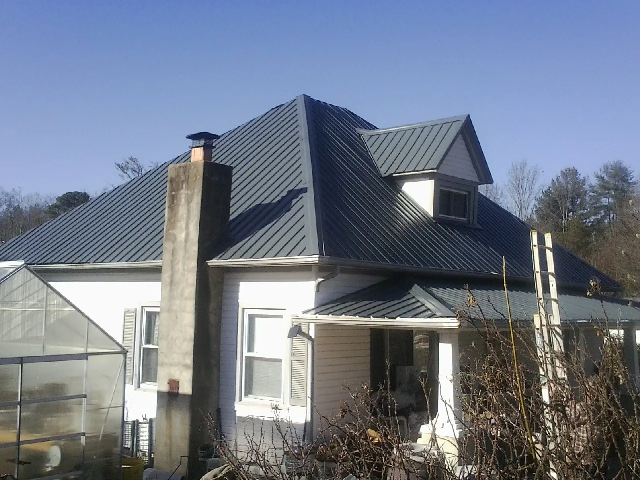 Dark blue standing seam metal roof on a white farmhouse with dormer — Slate & Tile Roof Repair by Roofing Brothers in La Fontaine