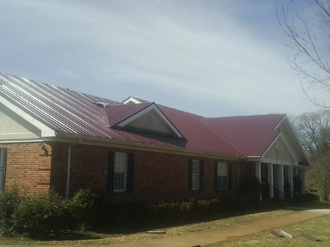 Red metal roof with gabled entries on a long brick building, from a Hail Damage Roof Repair job in La Fontaine