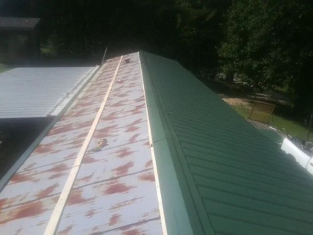Old rusted panels beside newly installed green metal roofing — Wind Damage Roof Repair by Roofing Brothers in La Fontaine