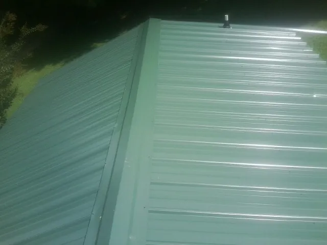 New green metal panels meeting at the ridge of a roof — Flat Roof Repair work by our crew in La Fontaine