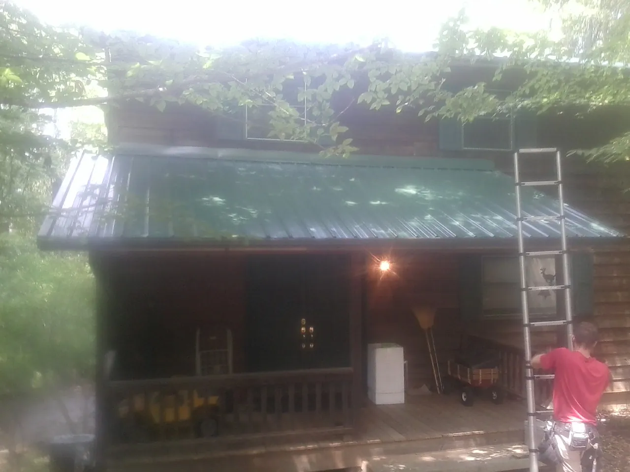 Worker on a ladder at the green porch roof of a wooded cabin in La Fontaine
