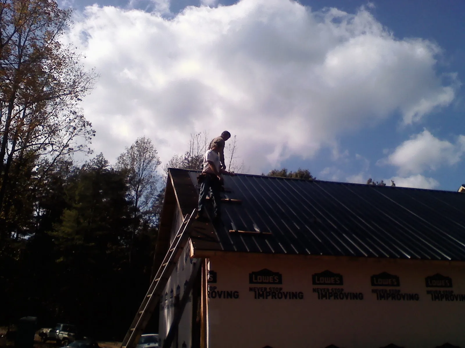 Roofer fastening dark metal panels high against a cloudy sky, from a Roof Inspection job in La Fontaine