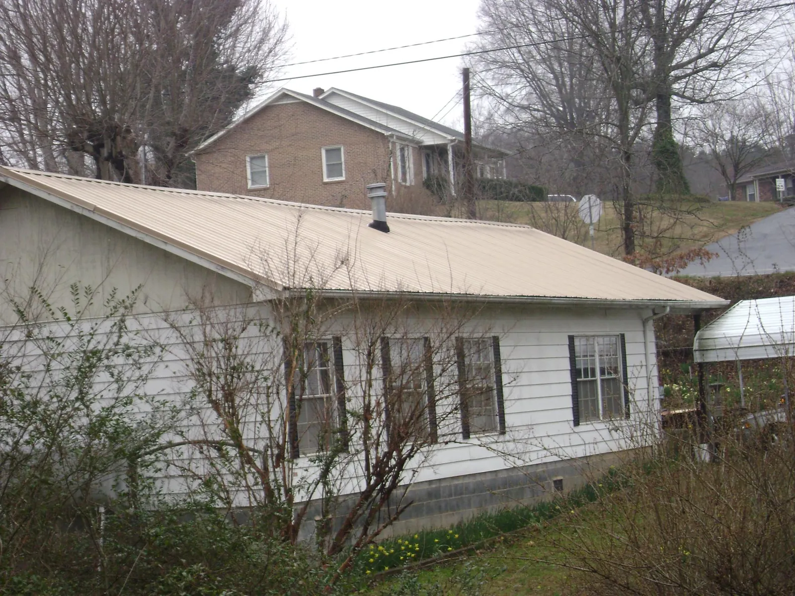 Tan metal roof on a white sided house set into a hillside — Commercial Roofing by Roofing Brothers in La Fontaine