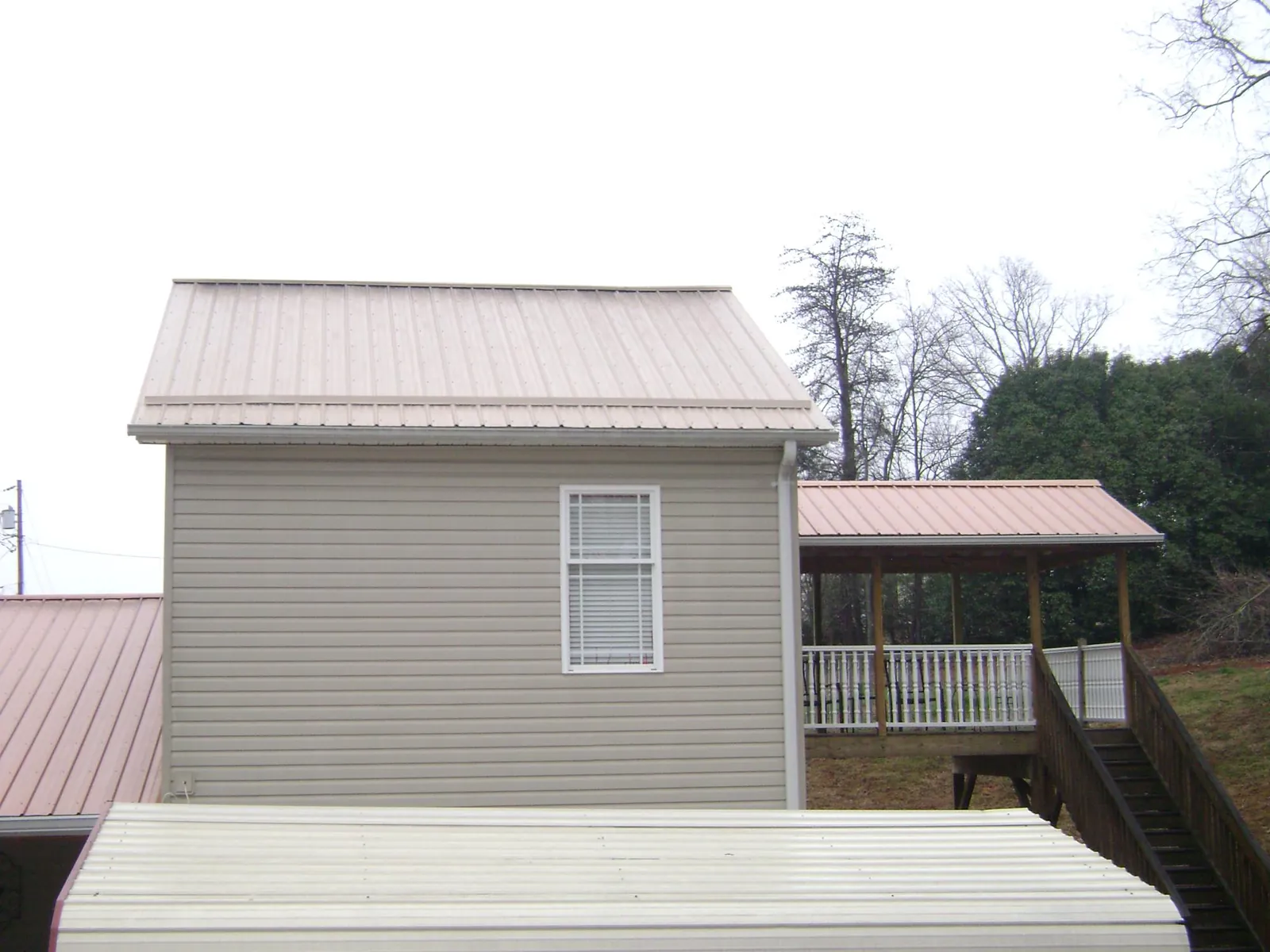 Tan metal roofs on a two story addition and attached porch, from a Roof Replacement job in La Fontaine